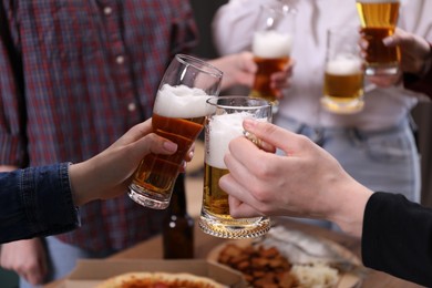 Photo of Friends clinking glasses of beer at table, closeup