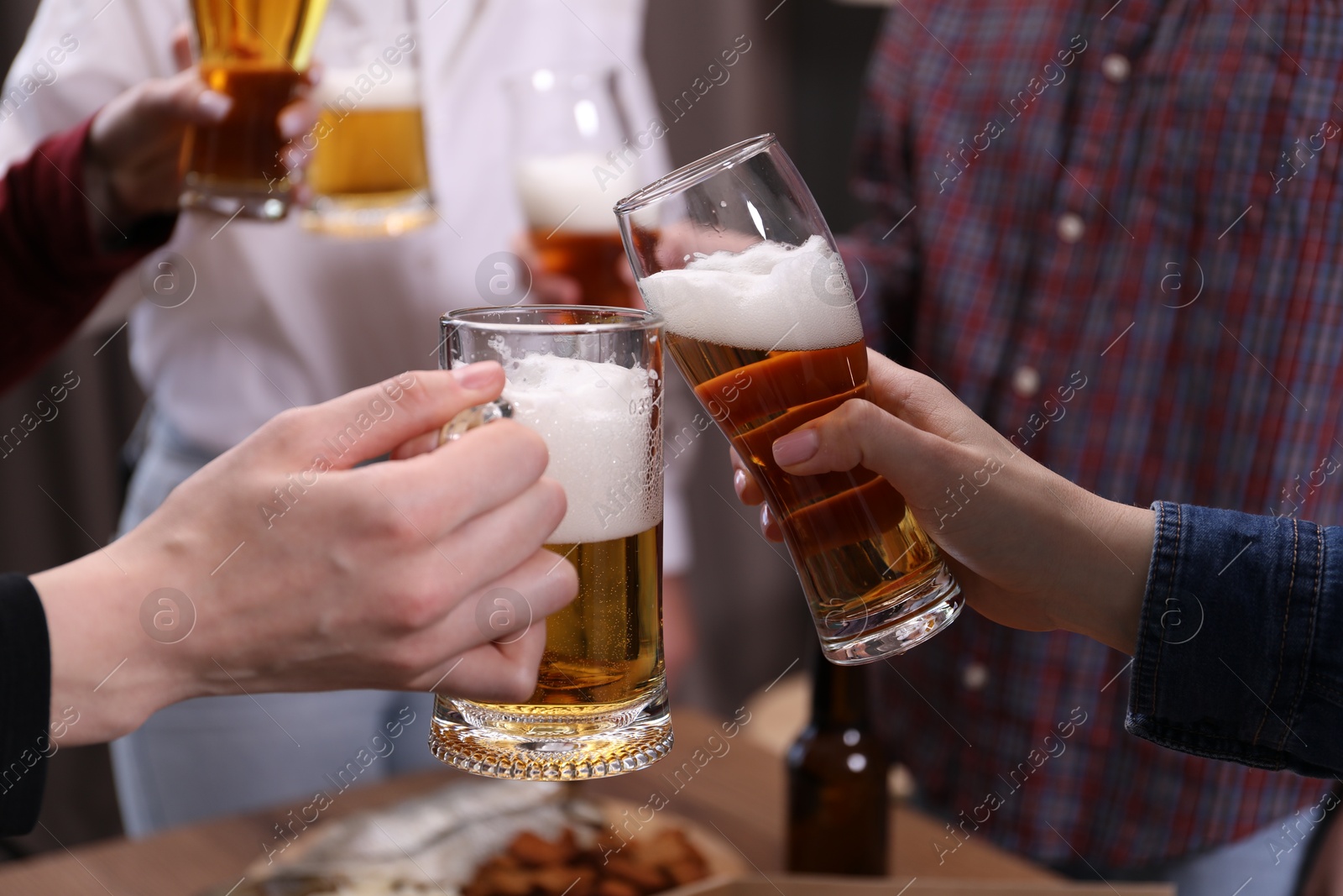 Friends clinking glasses of beer at table, closeup Photo of Friends clinking glasses of beer at table, closeup