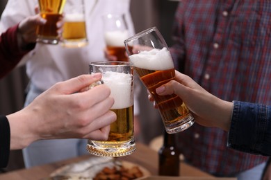 Photo of Friends clinking glasses of beer at table, closeup