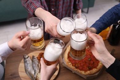 Photo of Friends clinking glasses of beer at wooden table, closeup
