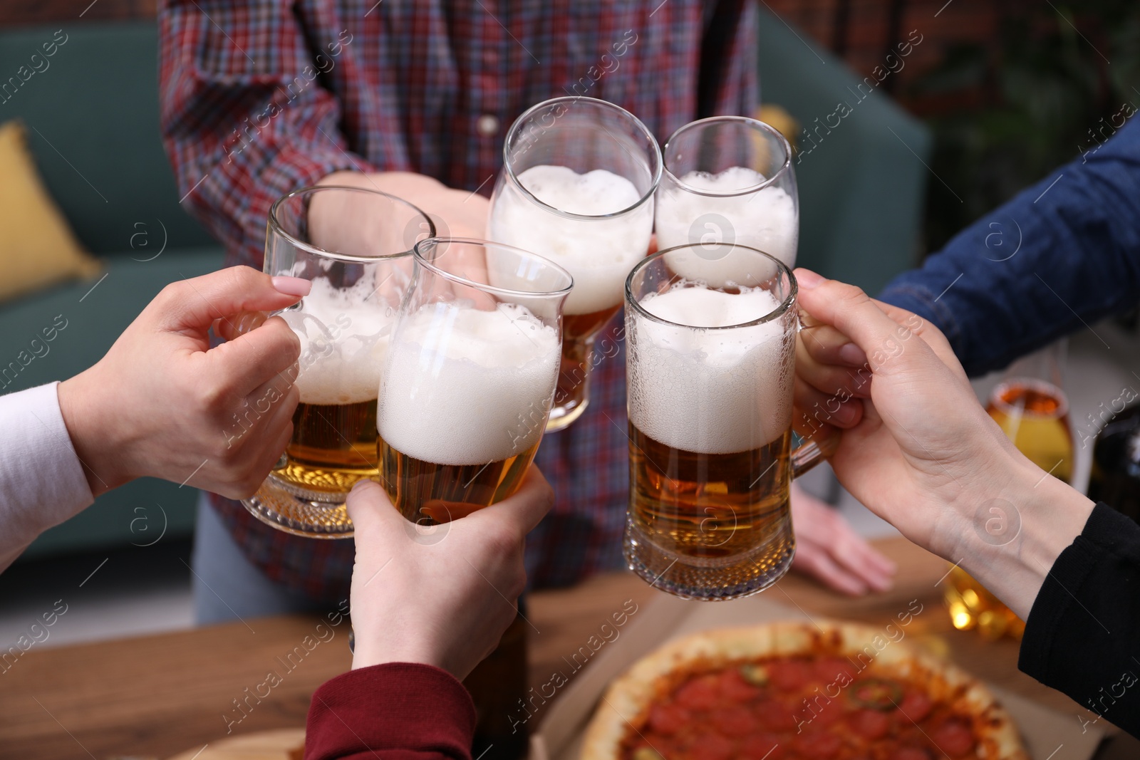Friends clinking glasses of beer at table, closeup Photo of Friends clinking glasses of beer at table, closeup
