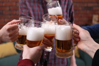 Photo of Friends clinking glasses of beer indoors, closeup