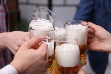 Photo of Friends clinking glasses of beer indoors, closeup