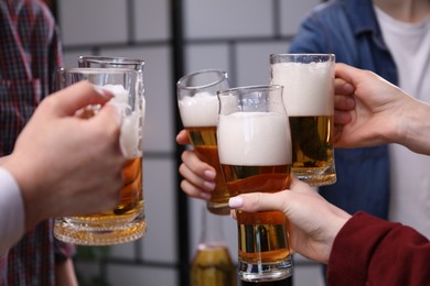Photo of Friends clinking glasses of beer indoors, closeup