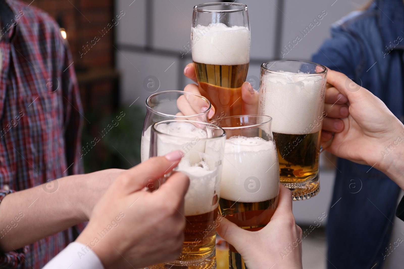 Friends clinking glasses of beer indoors, closeup Photo of Friends clinking glasses of beer indoors, closeup