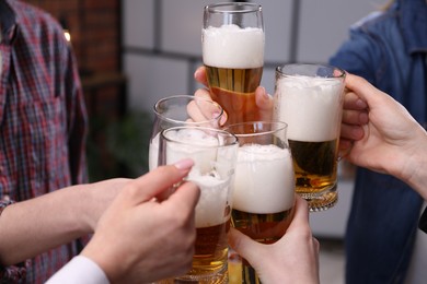 Photo of Friends clinking glasses of beer indoors, closeup