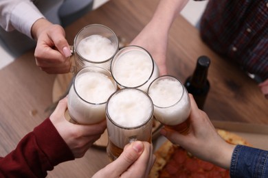 Photo of Friends clinking glasses of beer at wooden table, closeup