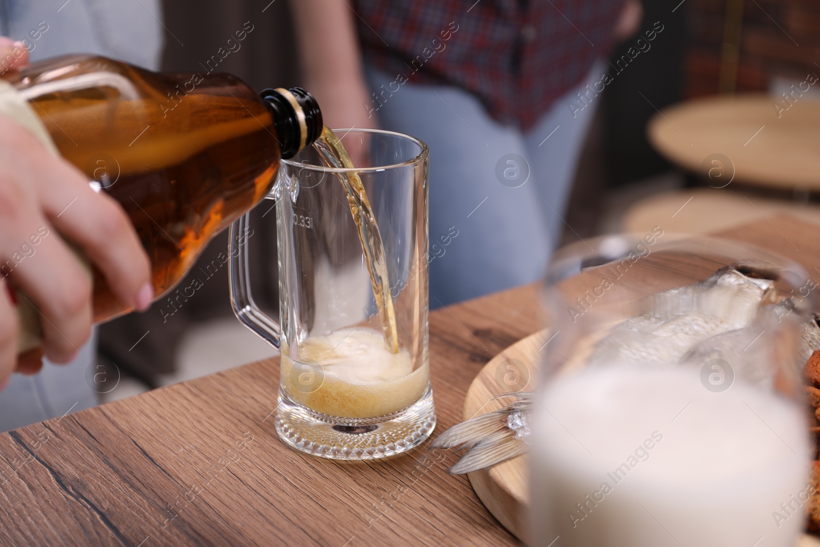 Woman pouring beer into glass at wooden table, closeup Photo of Woman pouring beer into glass at wooden table, closeup