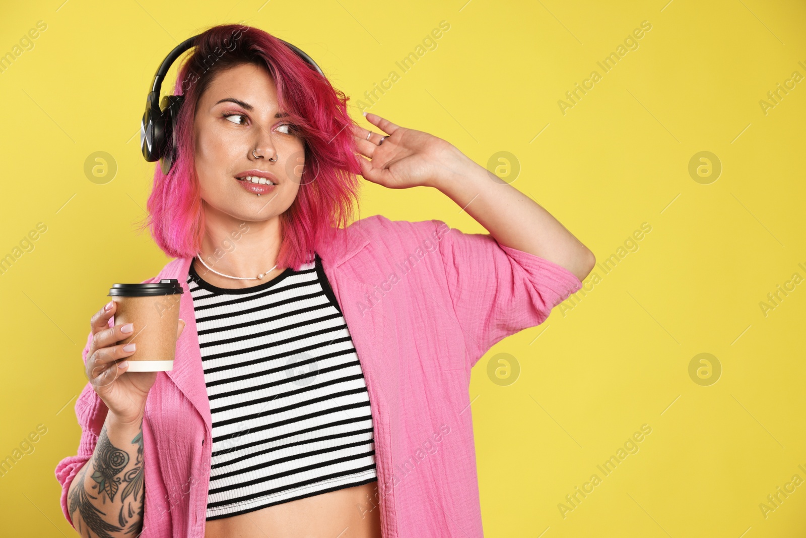 Beautiful woman with pink dyed hair and coffee listening to music on yellow background Photo of Beautiful woman with pink dyed hair and coffee listening to music on yellow background