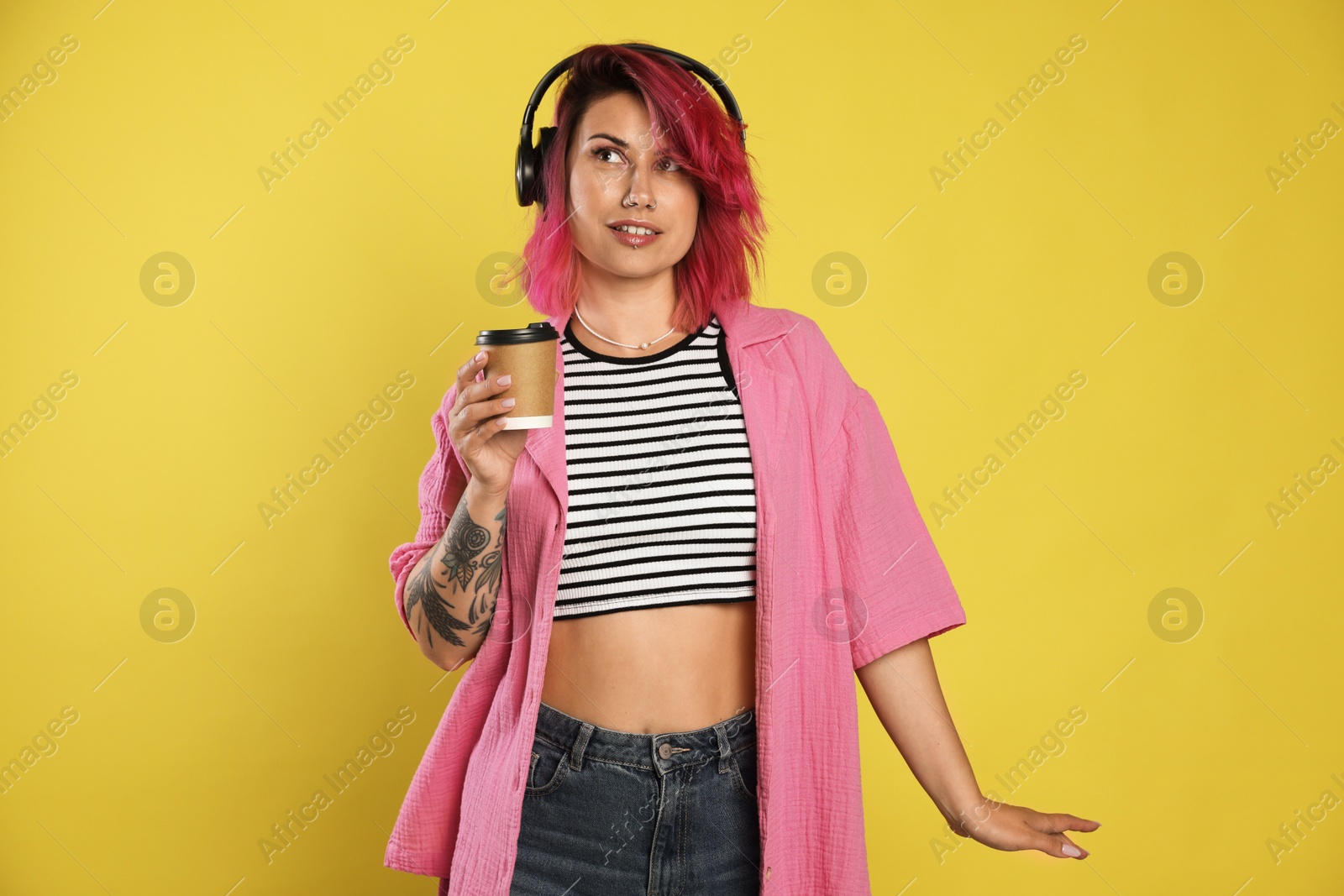 Beautiful woman with pink dyed hair and coffee listening to music on yellow background Photo of Beautiful woman with pink dyed hair and coffee listening to music on yellow background