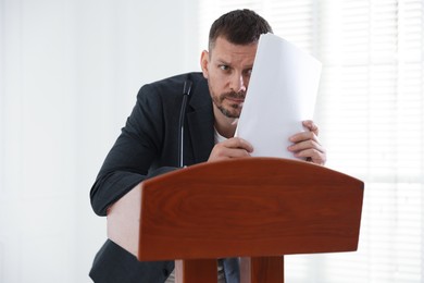 Photo of Fear of public speaking. Nervous man with microphone at lectern indoors
