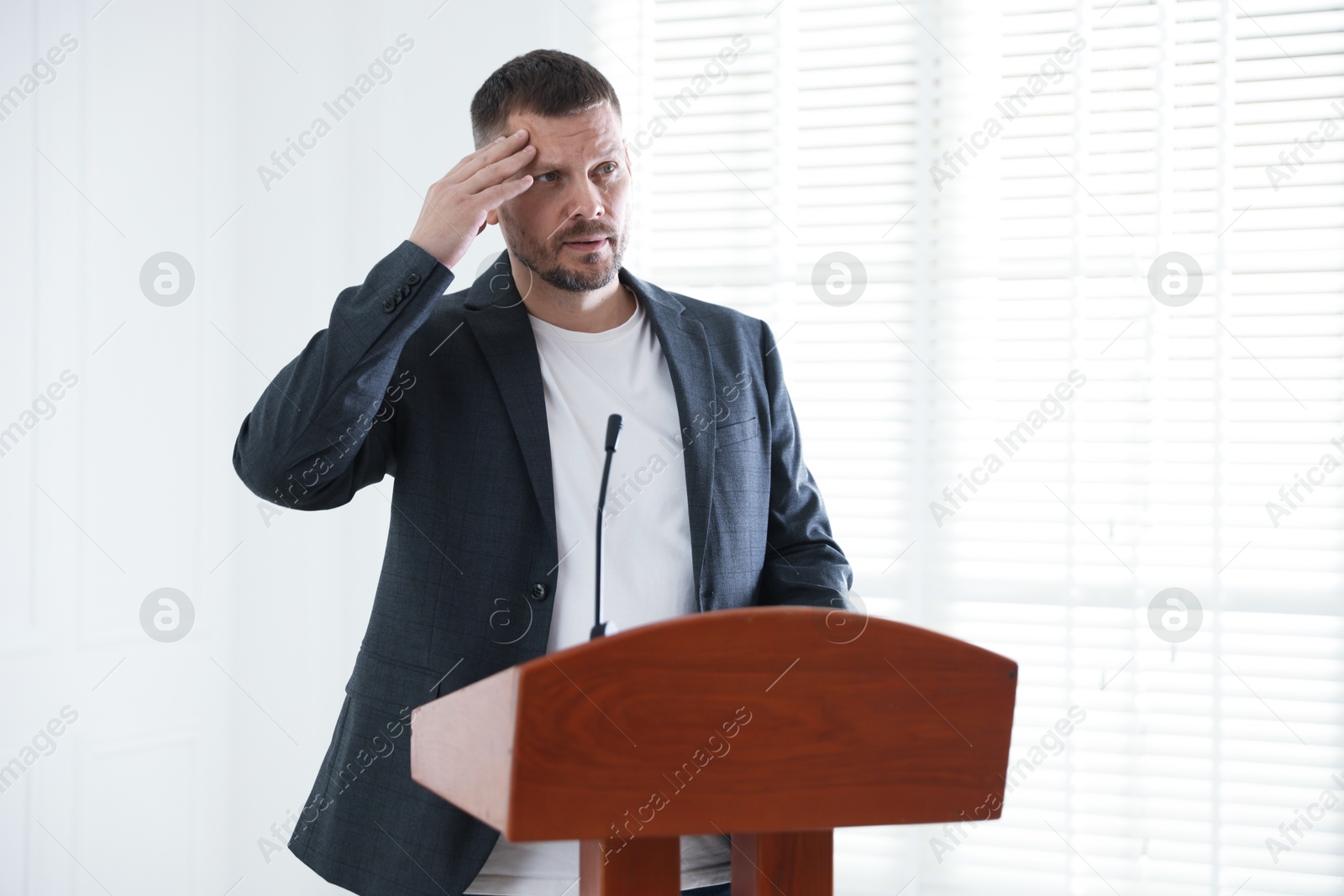 Photo of Fear of public speaking. Nervous man with microphone at lectern indoors