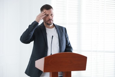 Photo of Fear of public speaking. Nervous man with microphone at lectern indoors