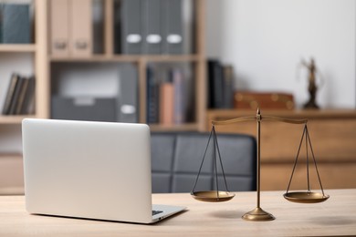 Photo of Scales of justice and laptop on wooden table in office