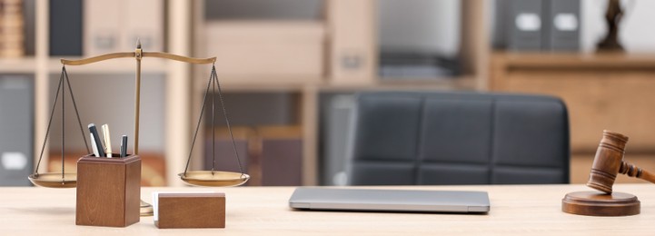 Photo of Judge's gavel, scales, laptop and stationery on wooden table in office