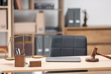 Photo of Judge's gavel, scales, laptop and stationery on wooden table in office