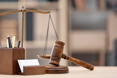 Photo of Judge's gavel, scales and stationery on wooden table in office