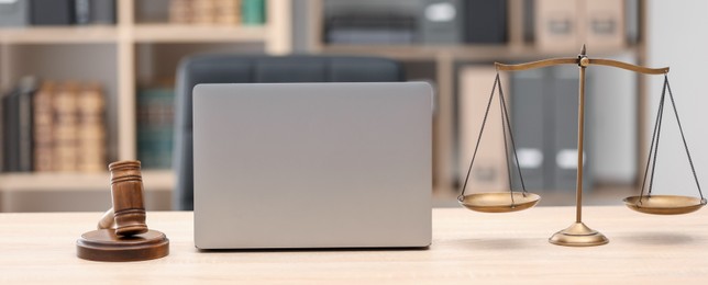 Photo of Judge's gavel, scales and laptop on wooden table in office