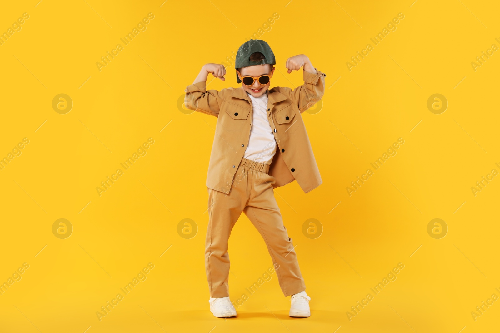 Happy little boy in sunglasses and baseball hat dancing on orange background Photo of Happy little boy in sunglasses and baseball hat dancing on orange background