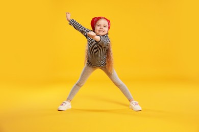 Photo of Cute little girl dancing on orange background