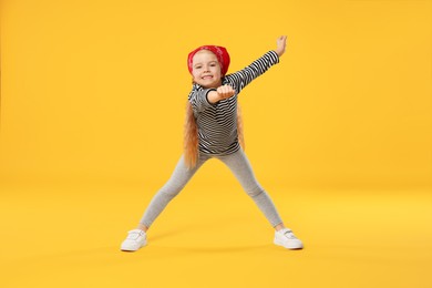 Photo of Cute little girl dancing on orange background