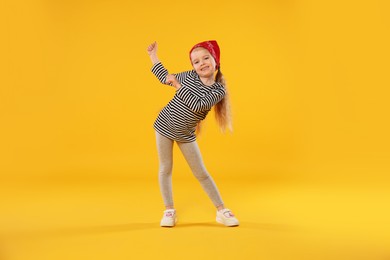 Photo of Cute little girl dancing on orange background