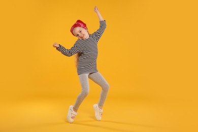 Photo of Cute little girl dancing on orange background