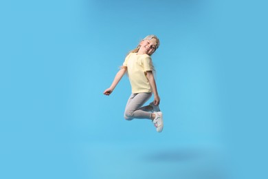 Photo of Cute little girl dancing on light blue background