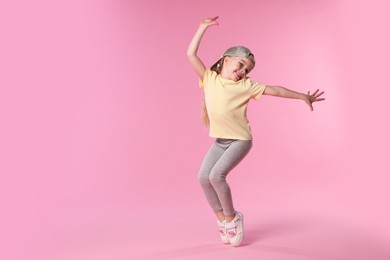 Photo of Cute little girl dancing on pink background, space for text