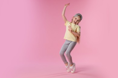 Photo of Cute little girl dancing on pink background, space for text