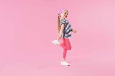 Photo of Cute little girl dancing on pink background