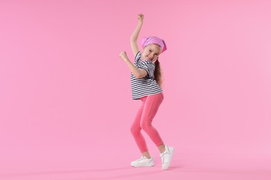 Photo of Cute little girl dancing on pink background
