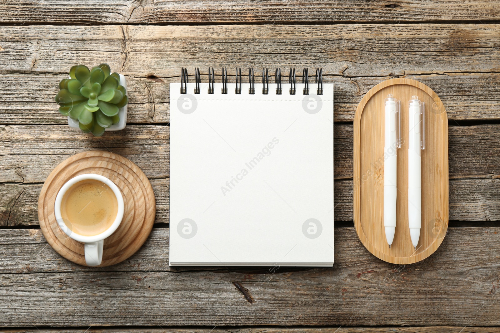 Photo of Open blank notebook, coffee, plant and pens on wooden table, flat lay