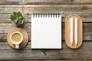 Photo of Open blank notebook, coffee, plant and pens on wooden table, flat lay
