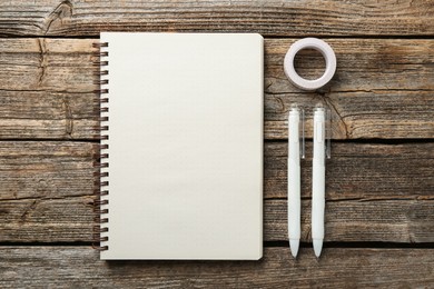 Photo of Open blank notebook, tape and pens on wooden table, flat lay