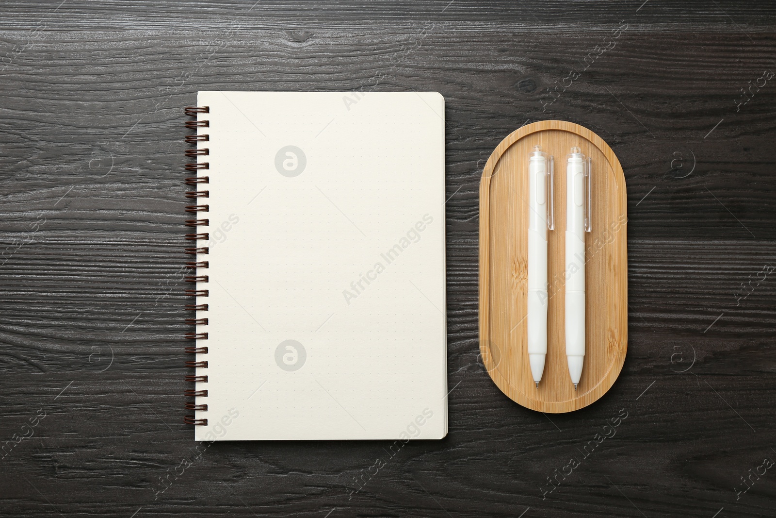 Photo of Open blank notebook and pens on black wooden table, top view