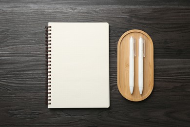 Photo of Open blank notebook and pens on black wooden table, top view