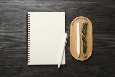 Photo of Open blank notebook, branch and pens on black wooden table, flat lay