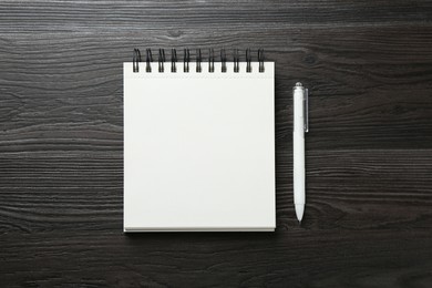 Photo of Open blank notebook and pen on black wooden table, top view