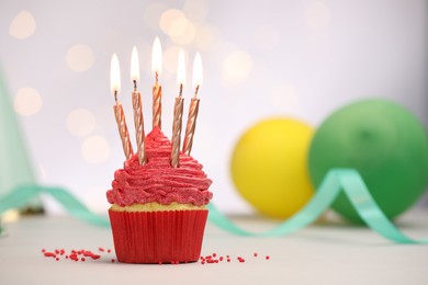 Photo of Burning candles in cupcake, sprinkles and party decor on white table against blurred lights, space for text