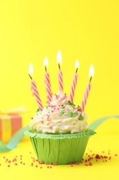 Photo of Burning candles in cupcake, sprinkles and party decor on yellow background