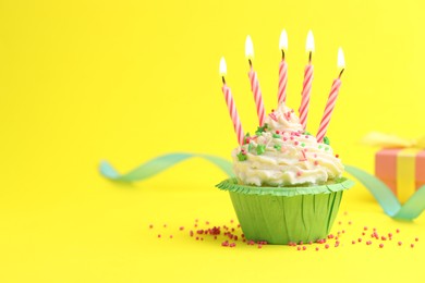 Photo of Burning candles in cupcake, sprinkles and party decor on yellow background, space for text