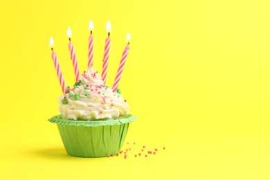 Photo of Burning candles in cupcake and sprinkles on yellow background, space for text