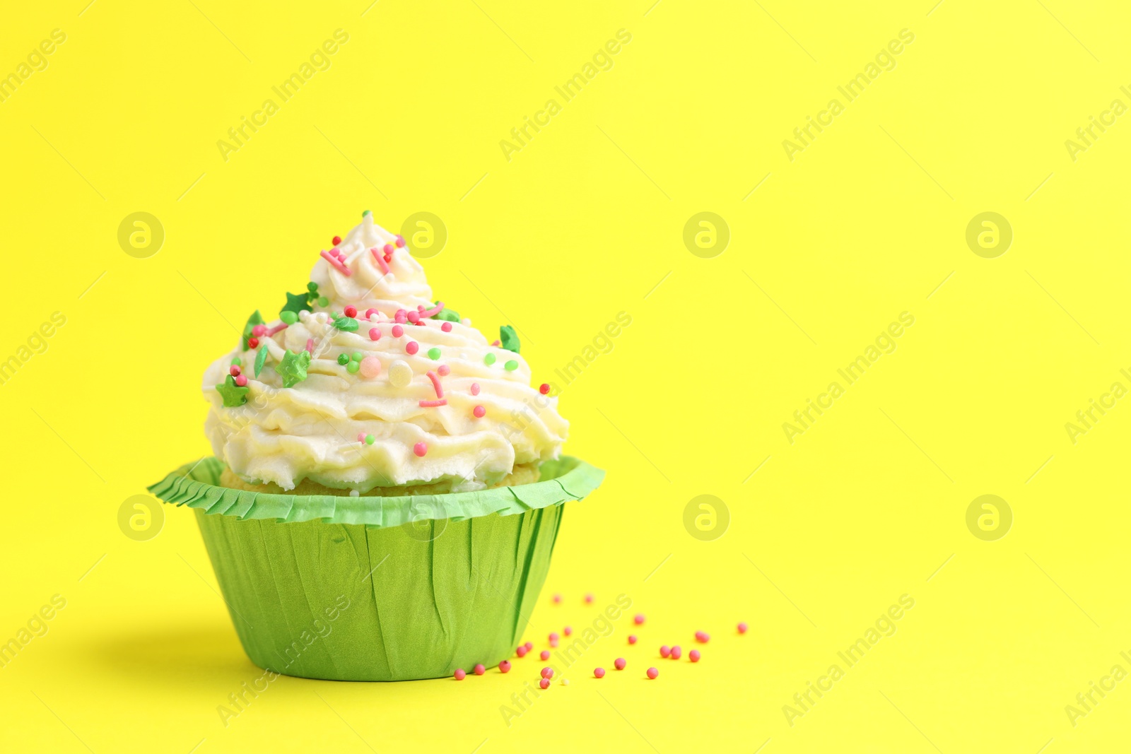 Photo of Tasty cupcake with sprinkles on yellow background, space for text