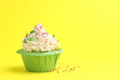 Photo of Tasty cupcake with sprinkles on yellow background, space for text