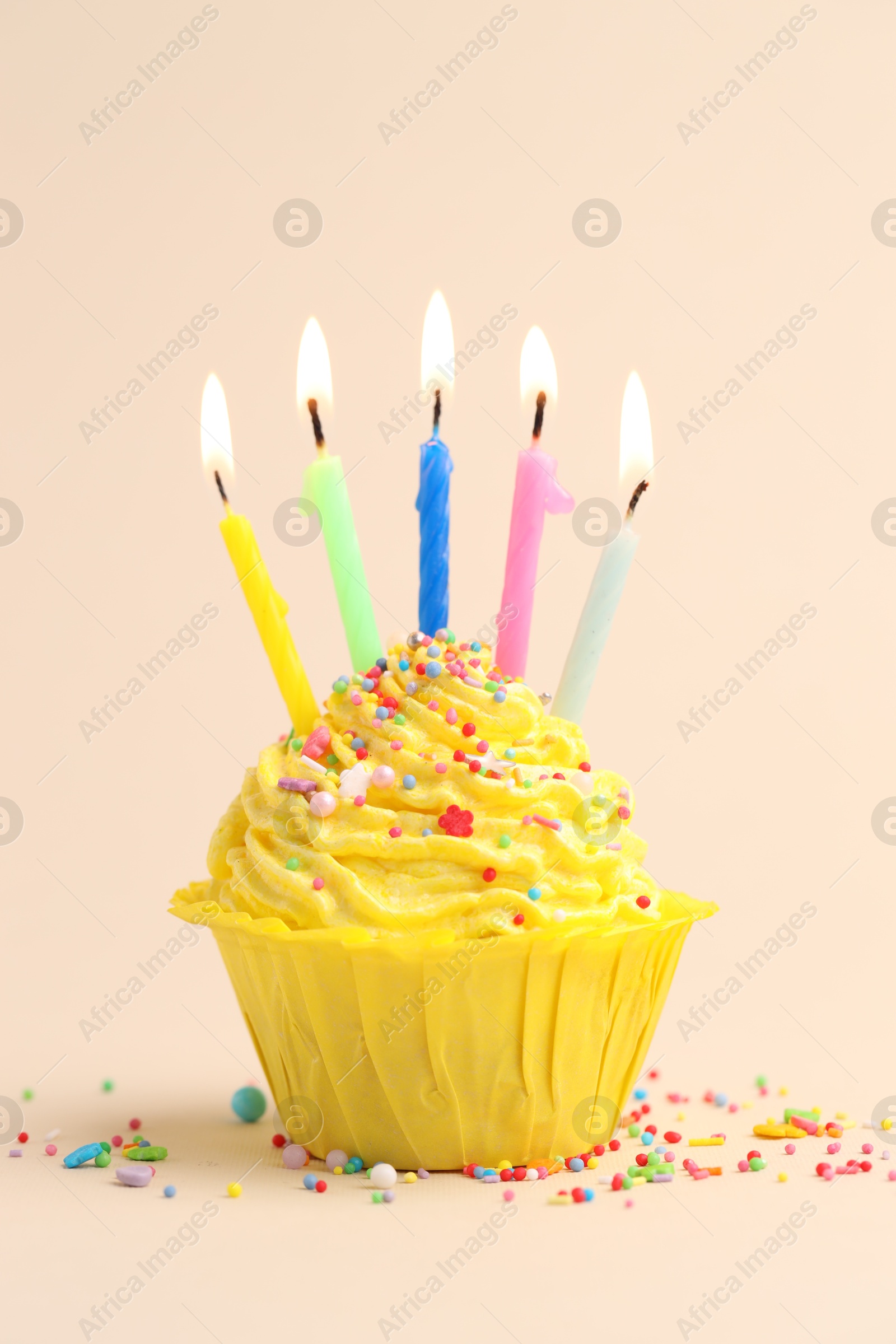 Photo of Burning candles in cupcake and sprinkles on beige background