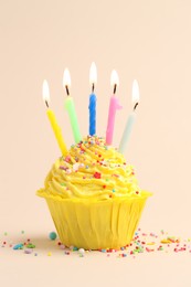 Photo of Burning candles in cupcake and sprinkles on beige background