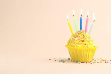 Photo of Burning candles in cupcake and sprinkles on beige background, space for text