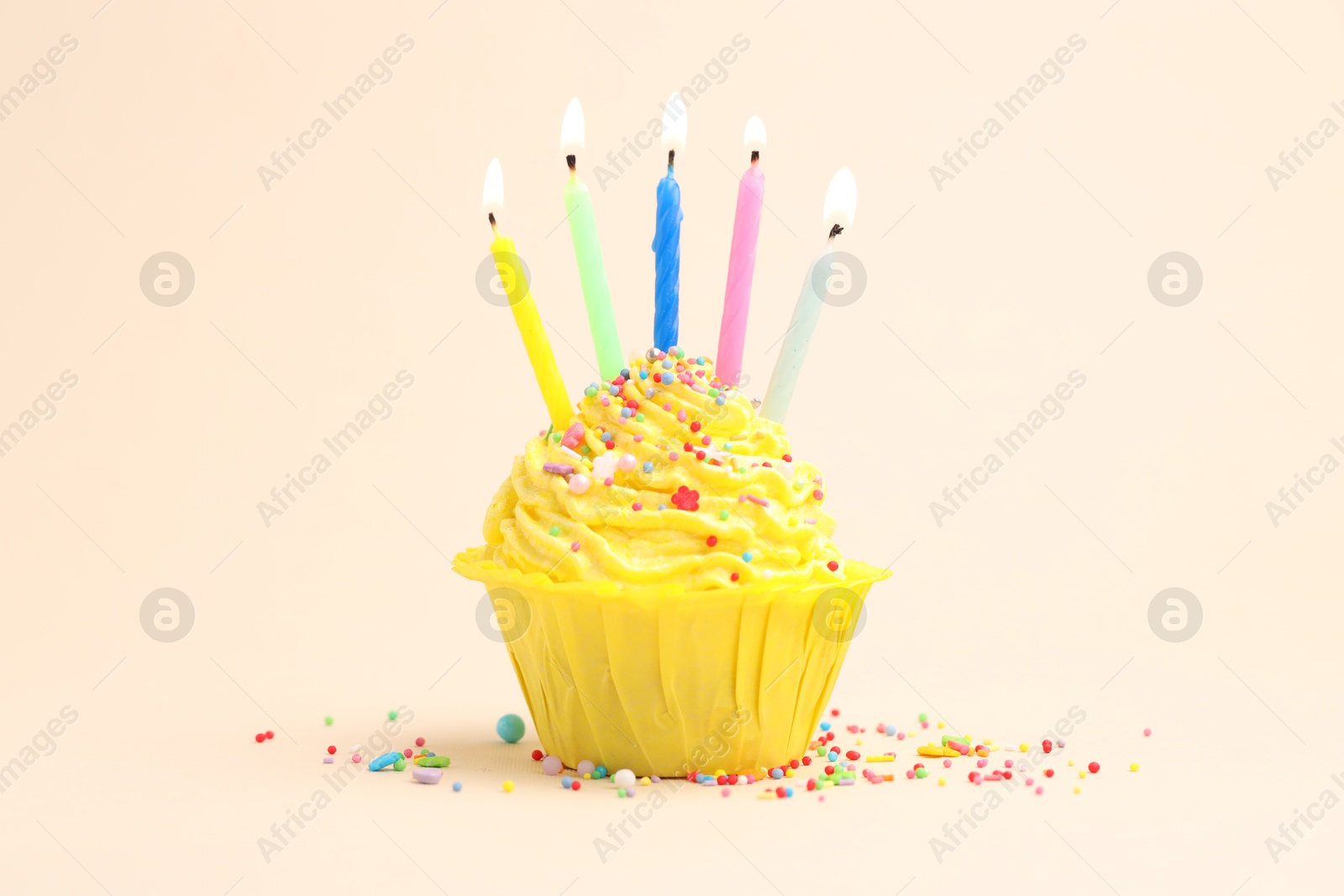 Burning candles in cupcake and sprinkles on beige background Photo of Burning candles in cupcake and sprinkles on beige background
