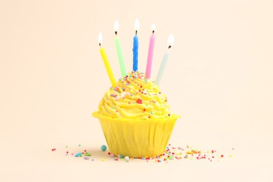 Photo of Burning candles in cupcake and sprinkles on beige background